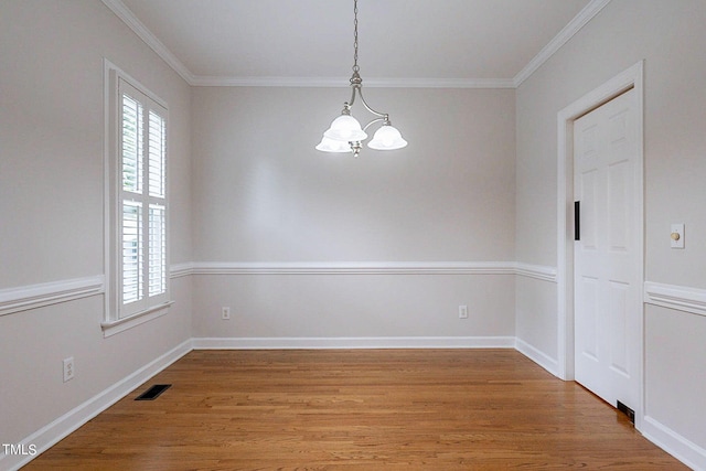 empty room featuring hardwood / wood-style floors, ornamental molding, and an inviting chandelier