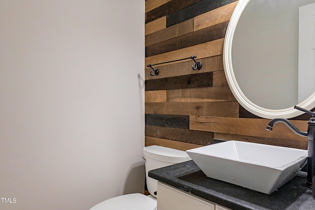 bathroom featuring toilet, vanity, and wooden walls