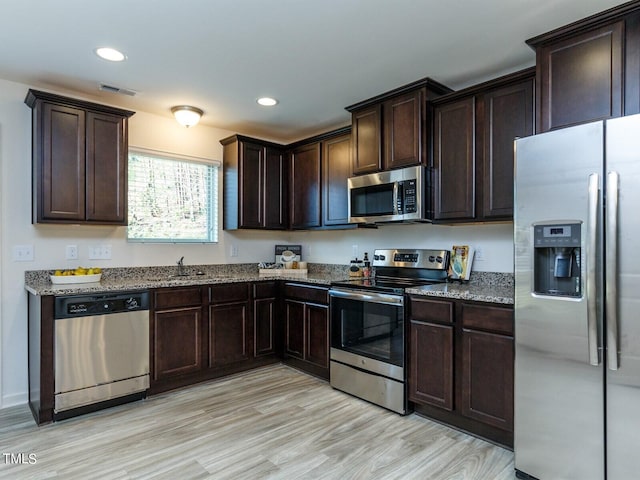 kitchen featuring light wood-type flooring, appliances with stainless steel finishes, light stone counters, and dark brown cabinets