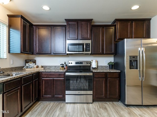 kitchen with appliances with stainless steel finishes, sink, light stone counters, light hardwood / wood-style flooring, and dark brown cabinets