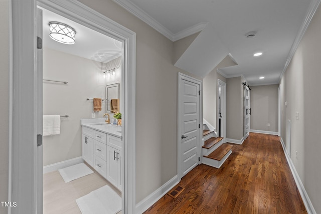 corridor featuring wood-type flooring, sink, a barn door, and ornamental molding