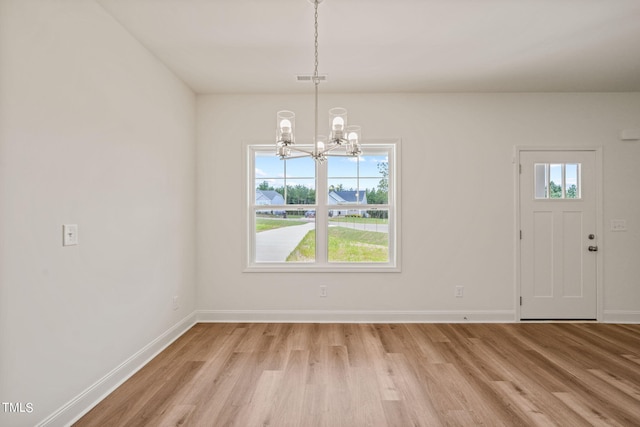 unfurnished dining area with light wood-type flooring, plenty of natural light, and an inviting chandelier