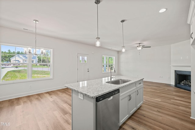 kitchen with dishwasher, white cabinetry, sink, light stone counters, and a center island with sink