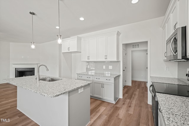 kitchen with pendant lighting, sink, white cabinetry, a kitchen island with sink, and range