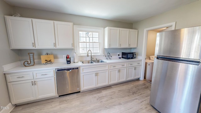 kitchen featuring washer / clothes dryer, white cabinetry, stainless steel appliances, sink, and light hardwood / wood-style flooring