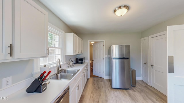 kitchen featuring sink, white cabinets, light wood-type flooring, and stainless steel fridge