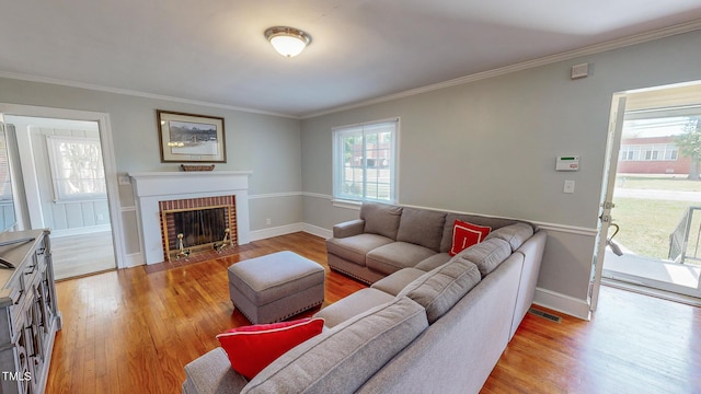 living room with light wood-type flooring, a brick fireplace, and crown molding