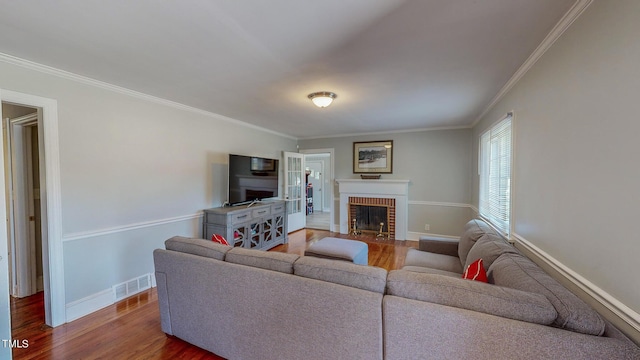 living room with a brick fireplace, hardwood / wood-style floors, and crown molding