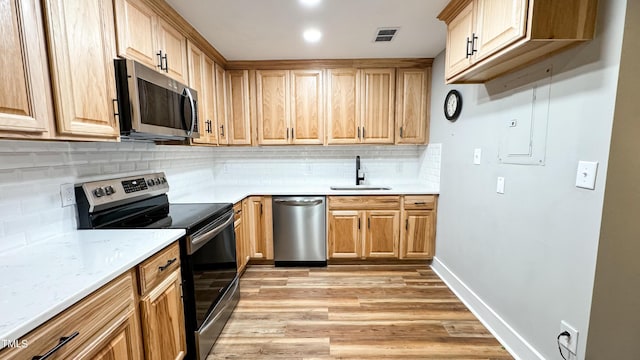 kitchen featuring sink, appliances with stainless steel finishes, light stone countertops, decorative backsplash, and light wood-type flooring