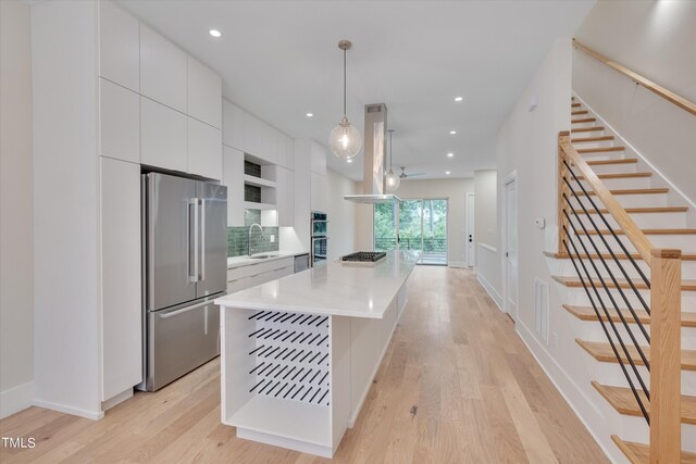 kitchen featuring decorative light fixtures, stainless steel appliances, light hardwood / wood-style floors, sink, and a kitchen island