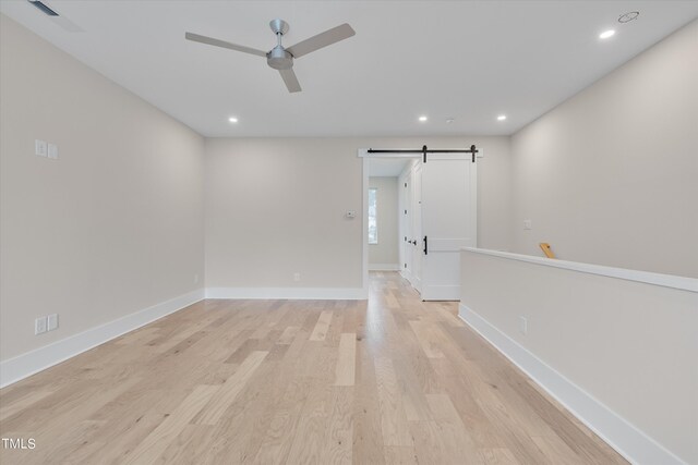 unfurnished room featuring a barn door, ceiling fan, and light hardwood / wood-style flooring