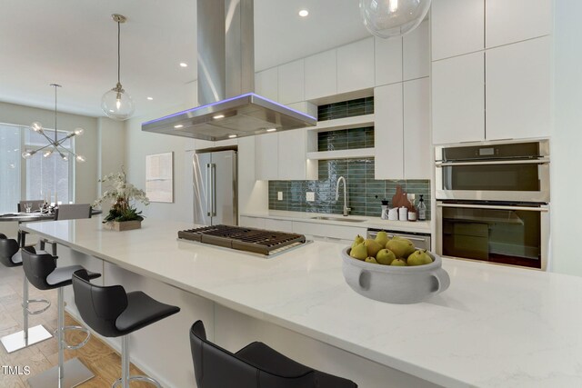 kitchen featuring a chandelier, backsplash, stainless steel appliances, sink, and island exhaust hood