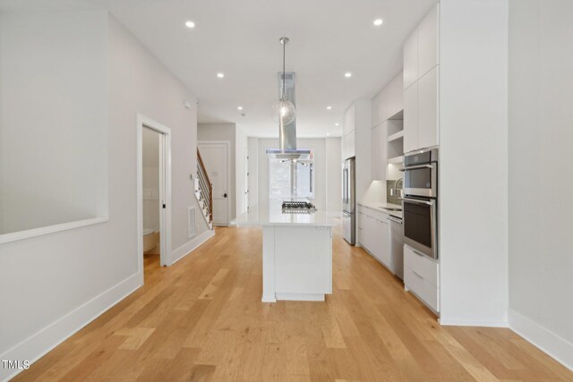 kitchen with a kitchen island, decorative light fixtures, white cabinets, and light hardwood / wood-style floors