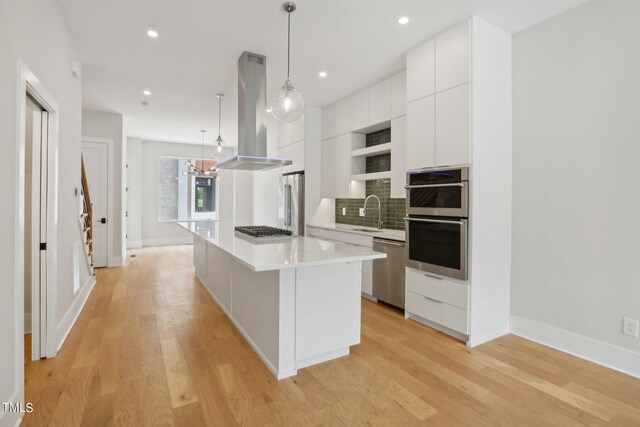 kitchen with a kitchen island, light hardwood / wood-style floors, island exhaust hood, hanging light fixtures, and white cabinets