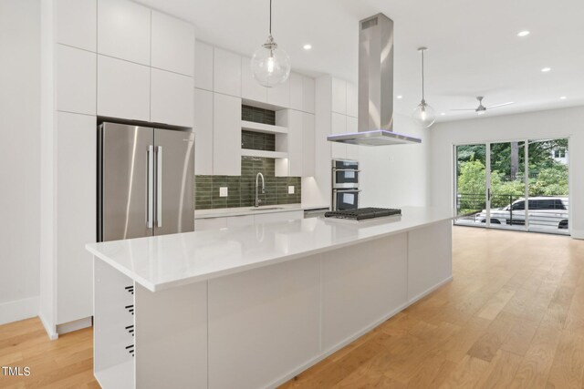 kitchen with light wood-type flooring, stainless steel appliances, sink, island exhaust hood, and a kitchen island