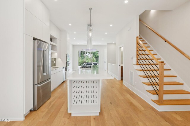 kitchen featuring stainless steel fridge, a center island, hanging light fixtures, white cabinets, and light hardwood / wood-style floors