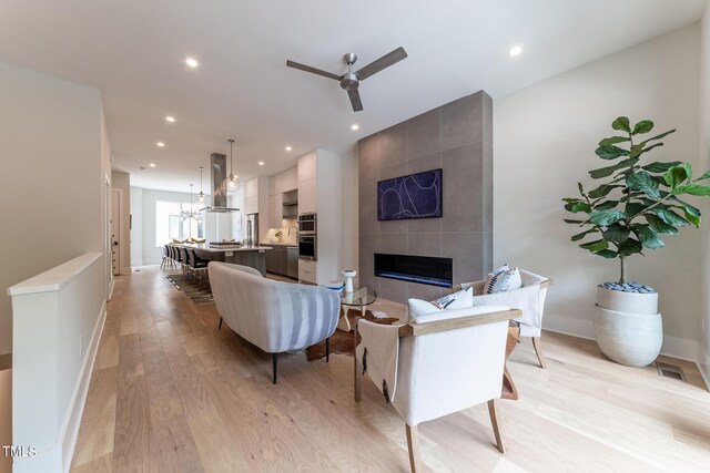 living room with light wood-type flooring, ceiling fan with notable chandelier, and a fireplace