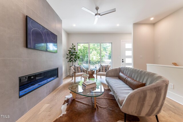 living room with light wood-type flooring, ceiling fan, and a tile fireplace