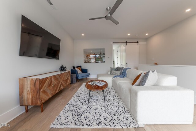 living room featuring a barn door, ceiling fan, and light wood-type flooring