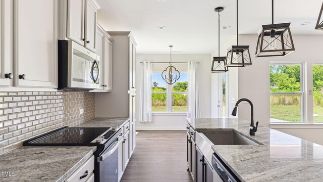 kitchen featuring sink, hanging light fixtures, stainless steel appliances, tasteful backsplash, and light stone counters