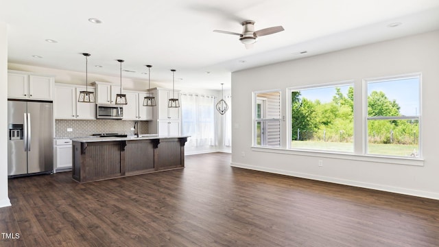 kitchen with stainless steel appliances, dark hardwood / wood-style floors, an island with sink, decorative light fixtures, and a breakfast bar area