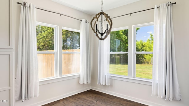 unfurnished dining area featuring a healthy amount of sunlight, dark hardwood / wood-style floors, and a notable chandelier