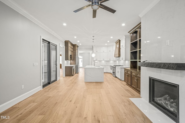 kitchen featuring white cabinets, an island with sink, pendant lighting, ornamental molding, and light hardwood / wood-style flooring