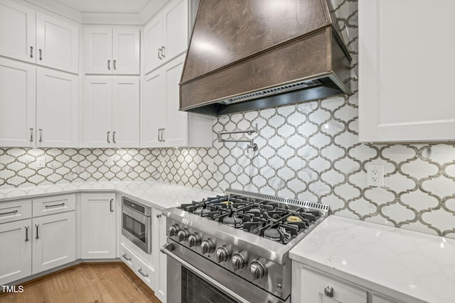 kitchen featuring white cabinetry, appliances with stainless steel finishes, tasteful backsplash, and premium range hood