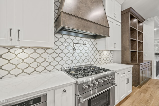 kitchen featuring light stone counters, light hardwood / wood-style floors, white cabinets, high end range, and premium range hood