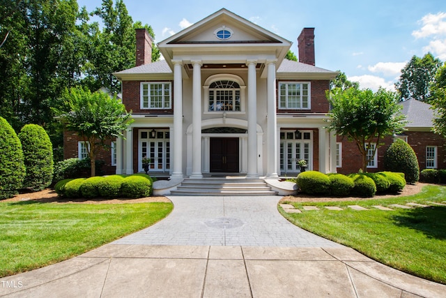 neoclassical home featuring french doors and a front lawn