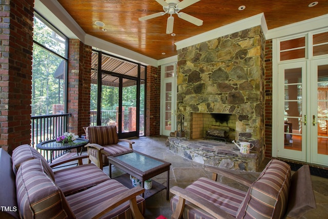 sunroom with a stone fireplace, ceiling fan, french doors, and wooden ceiling