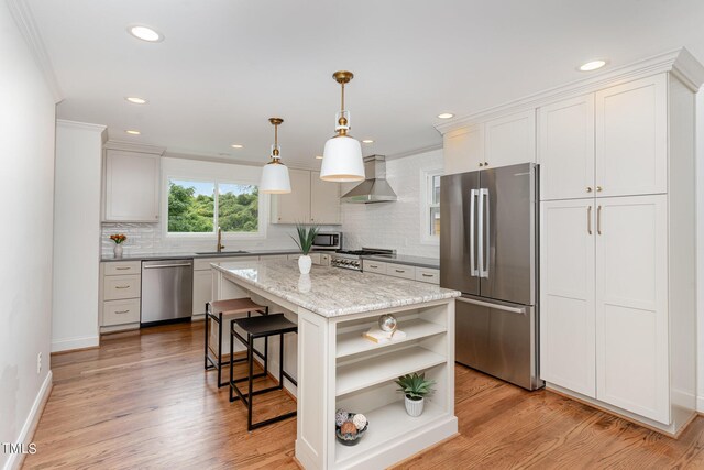 kitchen featuring wall chimney range hood, light hardwood / wood-style flooring, a kitchen island, backsplash, and appliances with stainless steel finishes