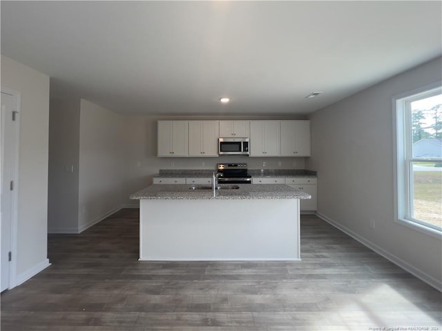 kitchen with appliances with stainless steel finishes, hardwood / wood-style floors, white cabinetry, and a center island with sink