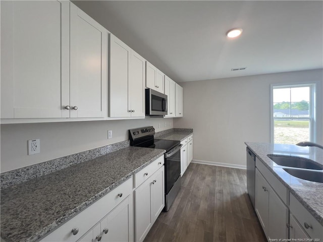 kitchen with dark stone countertops, sink, dark hardwood / wood-style floors, appliances with stainless steel finishes, and white cabinetry