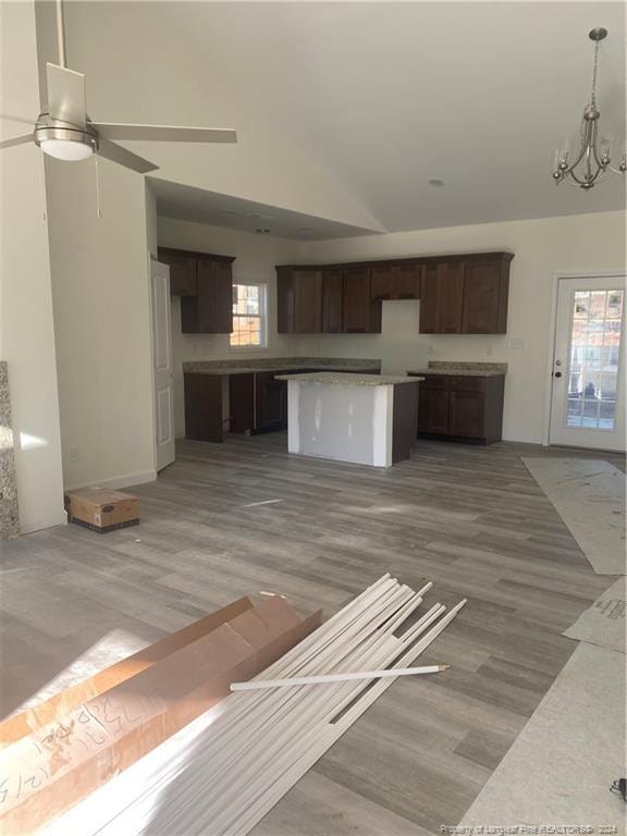 unfurnished living room with ceiling fan with notable chandelier, high vaulted ceiling, and light hardwood / wood-style flooring