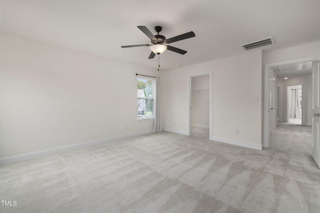 unfurnished bedroom featuring a closet, a walk in closet, ceiling fan, and light colored carpet