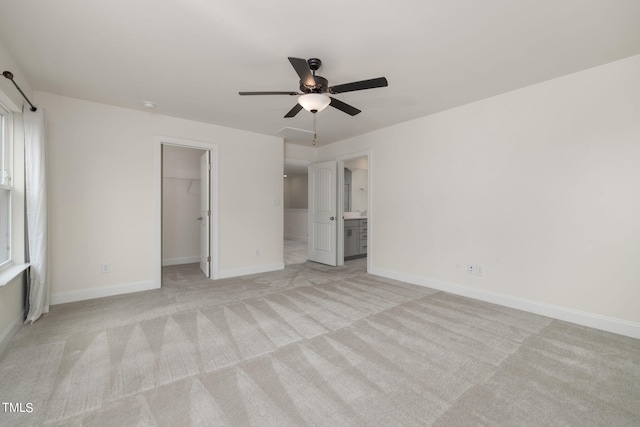 unfurnished bedroom with ceiling fan, light colored carpet, ensuite bathroom, a walk in closet, and a closet