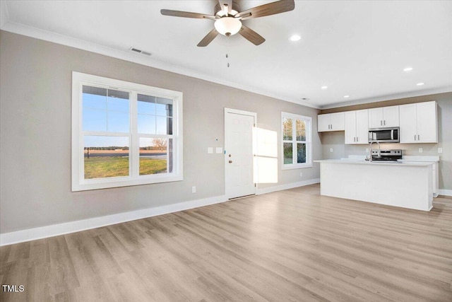 kitchen with white cabinets, ceiling fan, light wood-type flooring, ornamental molding, and appliances with stainless steel finishes