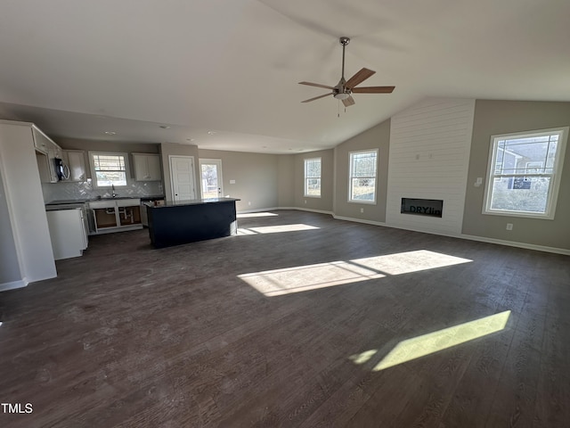 unfurnished living room with lofted ceiling, sink, a large fireplace, dark hardwood / wood-style floors, and ceiling fan