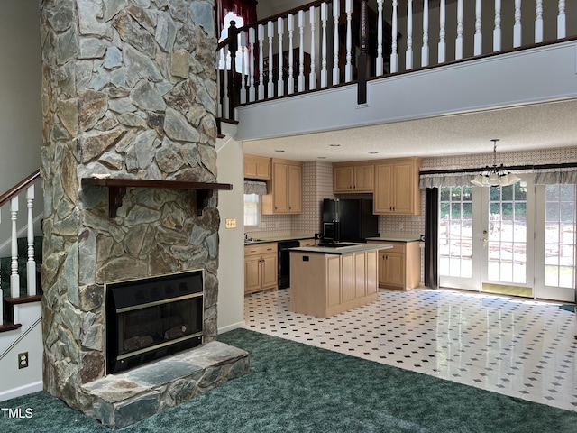 kitchen with black appliances, a kitchen island, light carpet, a stone fireplace, and light brown cabinets