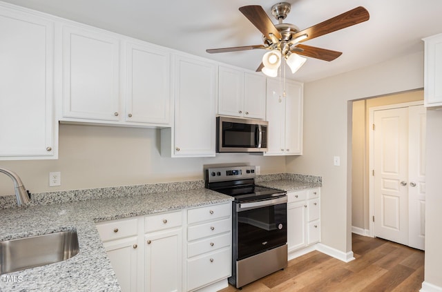 kitchen with white cabinetry, sink, ceiling fan, stainless steel appliances, and light stone counters