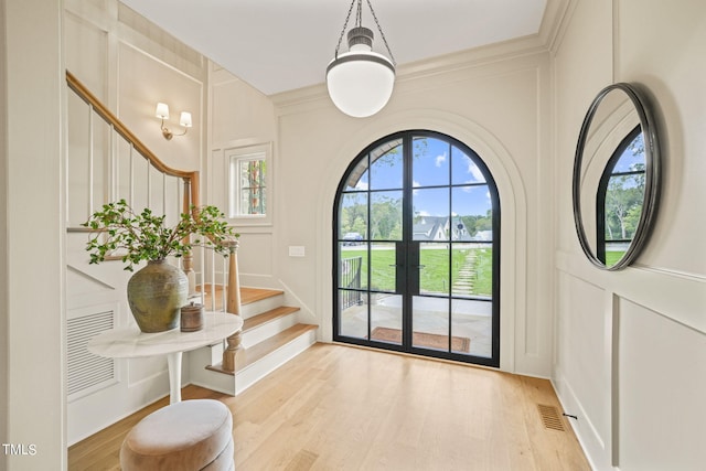 foyer entrance featuring french doors, light wood-type flooring, stairway, a decorative wall, and visible vents