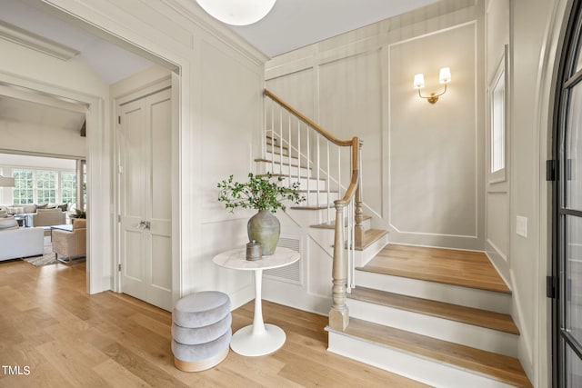 foyer featuring stairway, a decorative wall, and wood finished floors