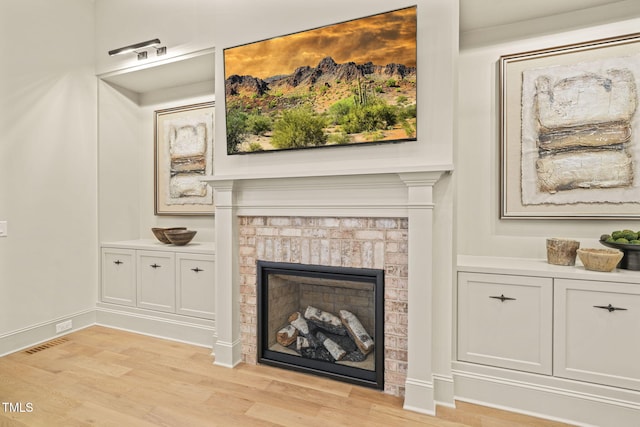 living room with light wood-style floors, visible vents, a fireplace, and baseboards