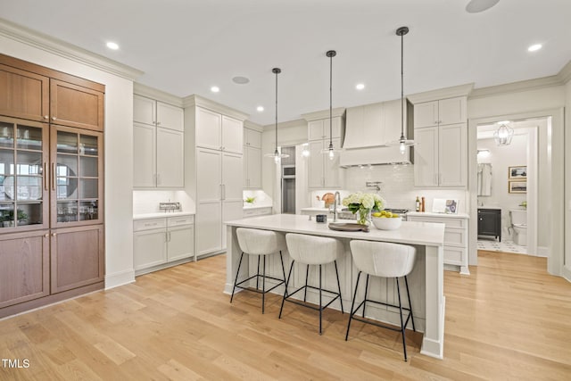 kitchen with a breakfast bar, a kitchen island with sink, backsplash, light countertops, and custom exhaust hood