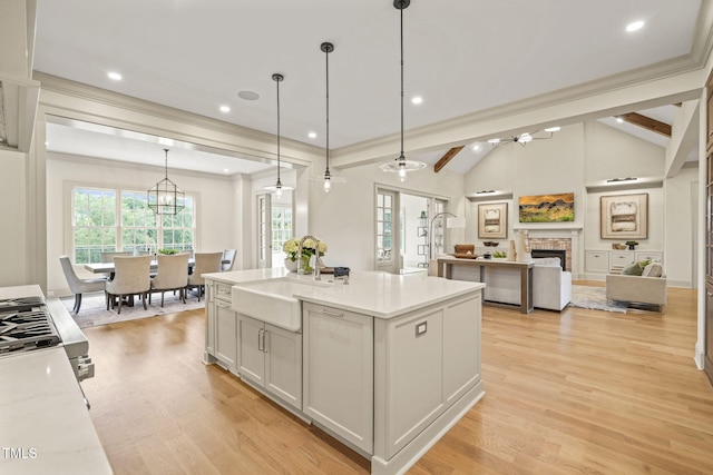 kitchen featuring a sink, light wood-type flooring, lofted ceiling with beams, and a stone fireplace