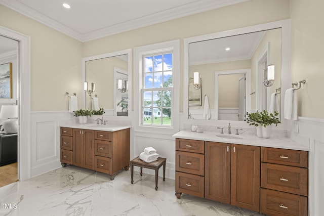 bathroom featuring a wainscoted wall, crown molding, a decorative wall, and a sink