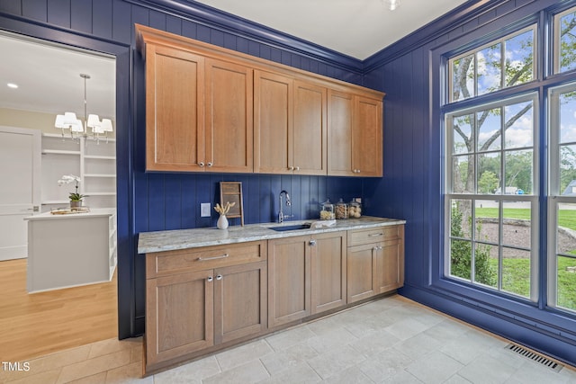 kitchen featuring a notable chandelier, light stone counters, visible vents, a sink, and crown molding
