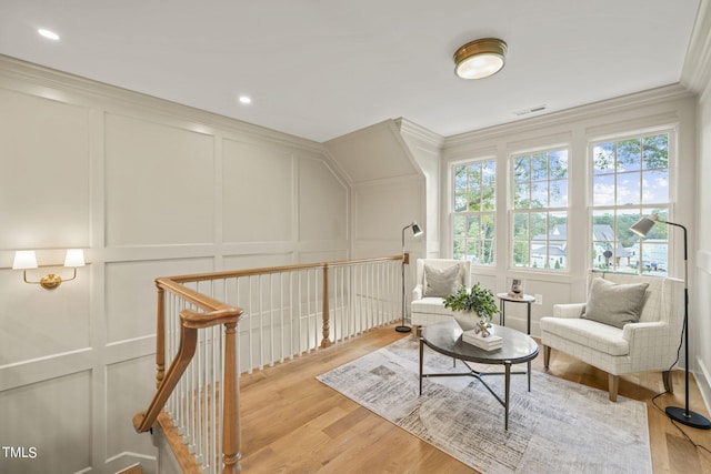 living area featuring a decorative wall, an upstairs landing, visible vents, crown molding, and light wood finished floors