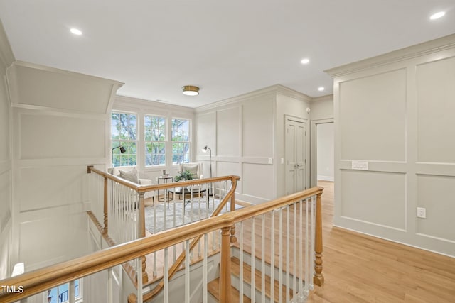 corridor with a decorative wall, ornamental molding, an upstairs landing, recessed lighting, and light wood-style floors